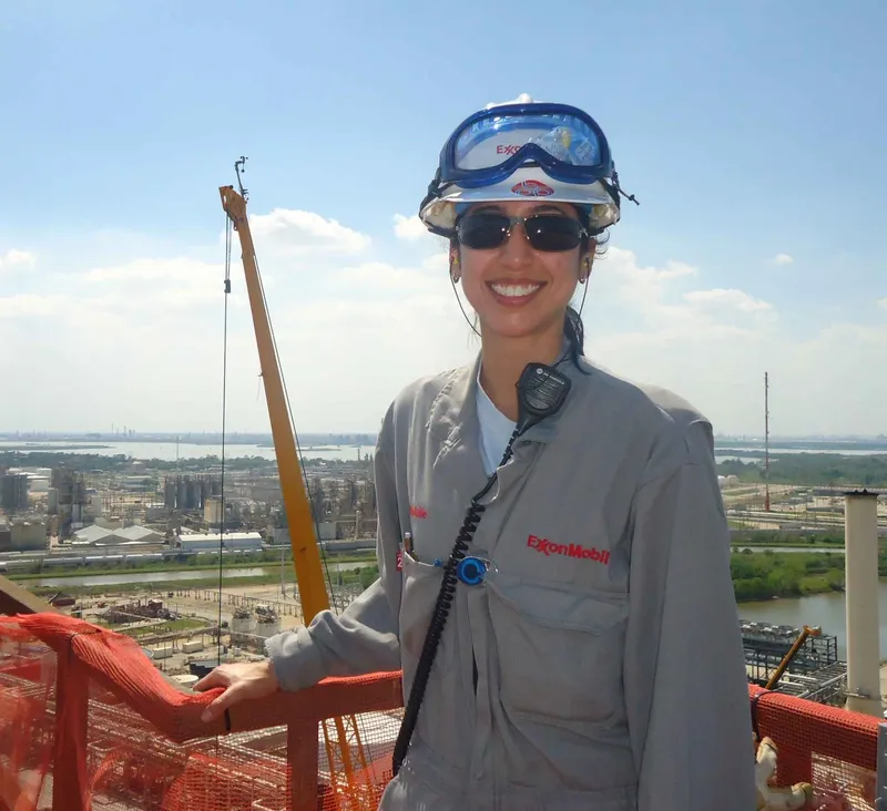 Natalie in an Exxon Mobil uniform, standing in front of a crane. 