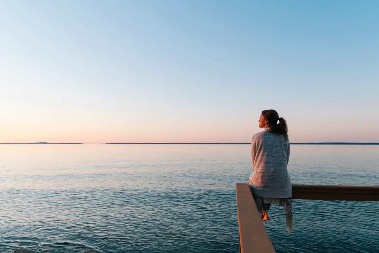 A woman sitting on a deck overlooking a large body of water