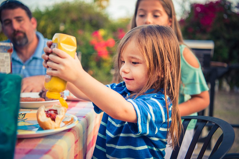 Boy squeezing mustard on hot dog.