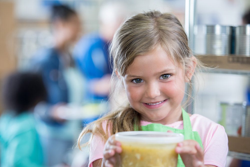 Little girl holding plastic soup container.