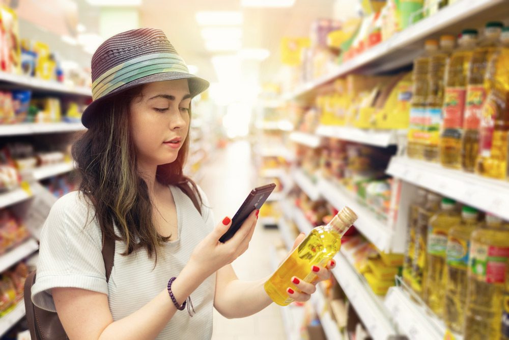 Woman holds plastic bottle and takes picture on cell phone.