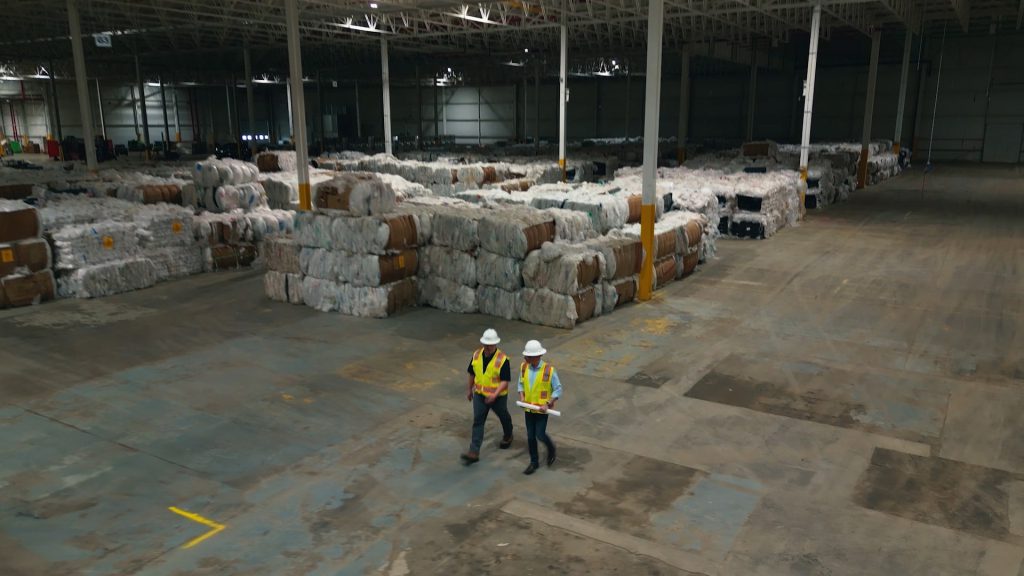 two works walking in a warehouse with plastic wrapping