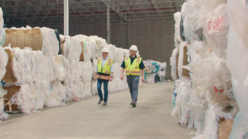 two men walking in a warehouse by plastic wrapping