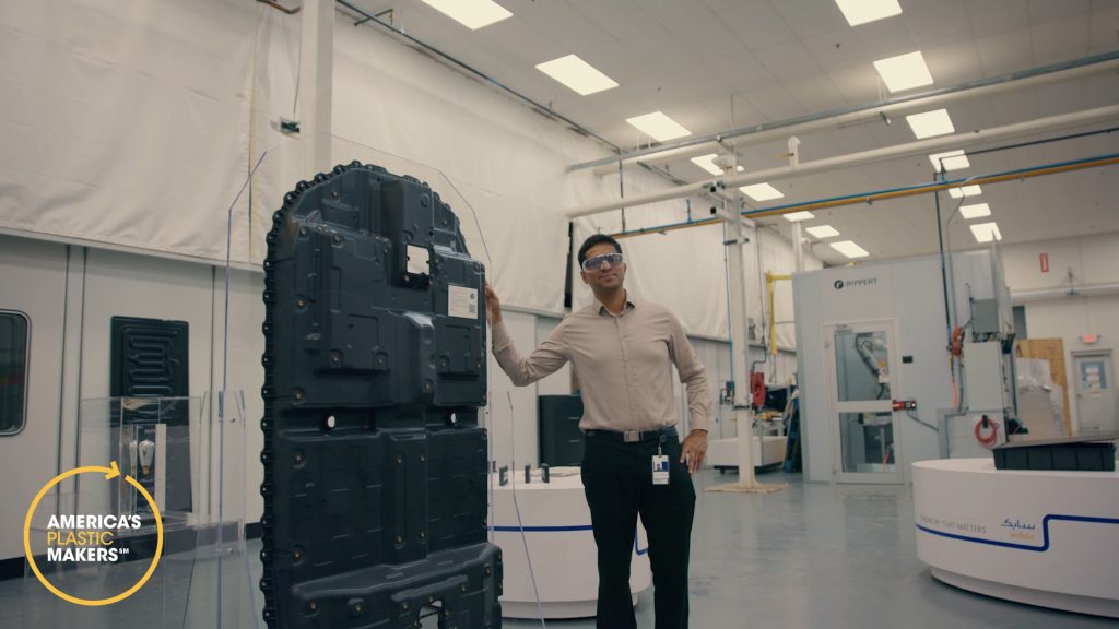 Dinesh standing next to a plastic piece used in a electric vehicle. 