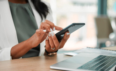 Woman holding cell phone next to laptop.