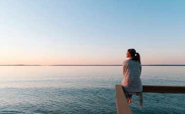 A woman sitting on a deck overlooking a large body of water